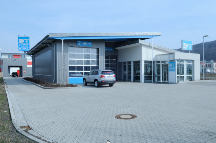 Ein modernes Autowerkstattzentrum mit blau-weißer Fassade, einem geparkten Auto und einem Schild mit dem Logo von "TUEV Hessen".