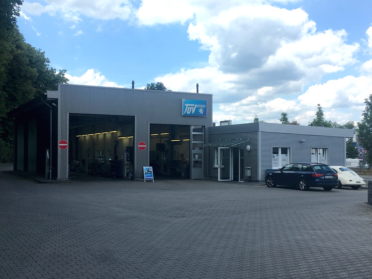 Eine Autowerkstatt mit einem "TUEV Hessen" Schild, einem Parkplatz und ein paar geparkten Autos.